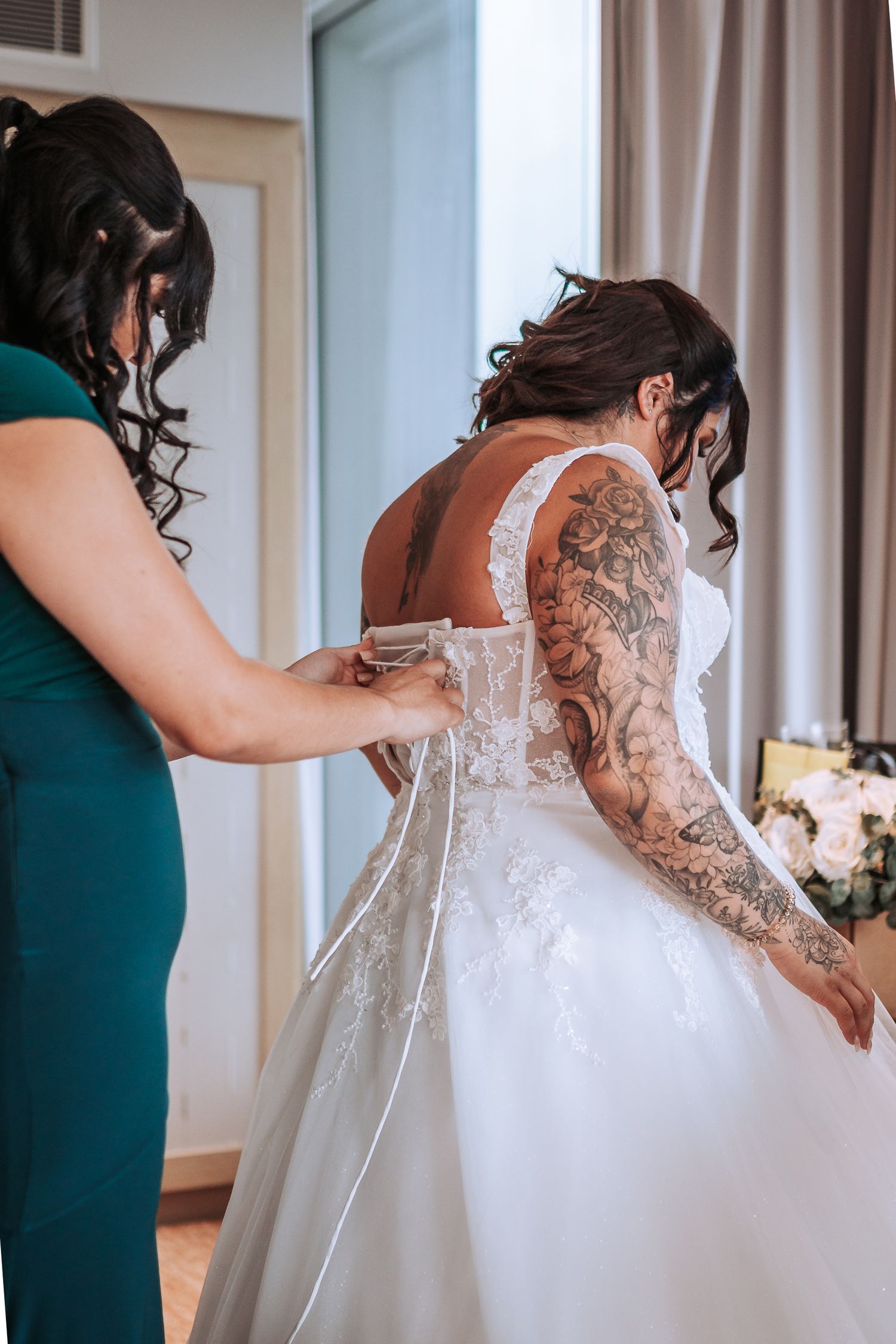 Close-up of intricate lacing detail on back of wedding dress with visible tattoo sleeve.