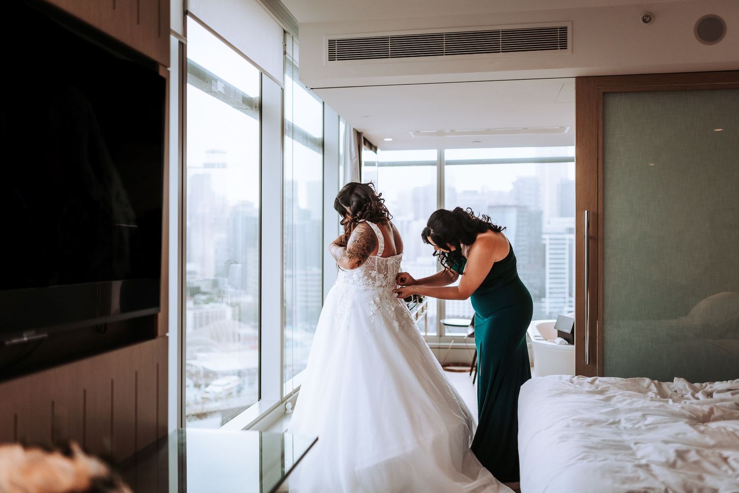 Wedding dress fitting session in modern hotel room with city views.