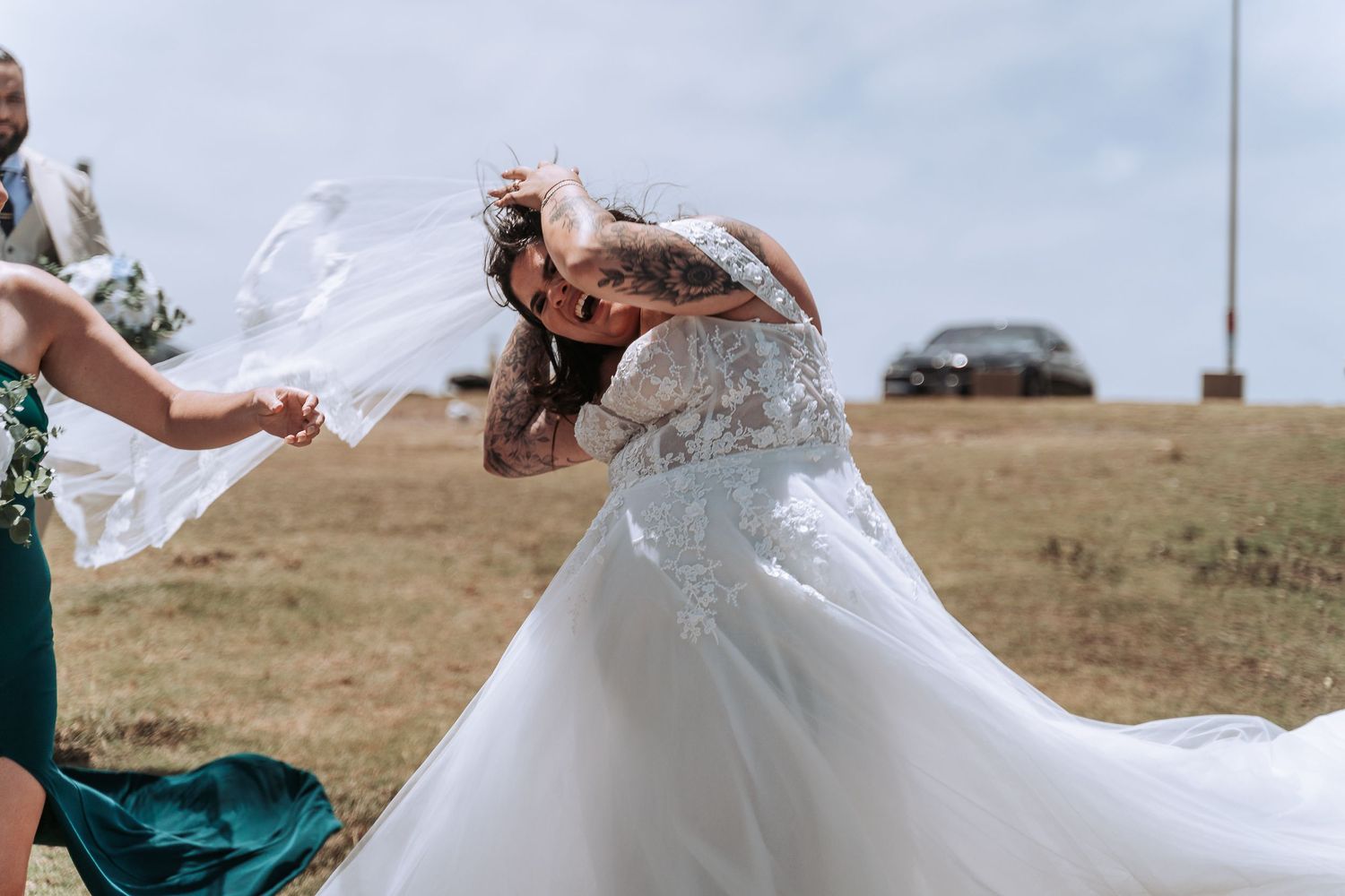 Wedding dress and veil caught in dramatic coastal wind during outdoor ceremony.