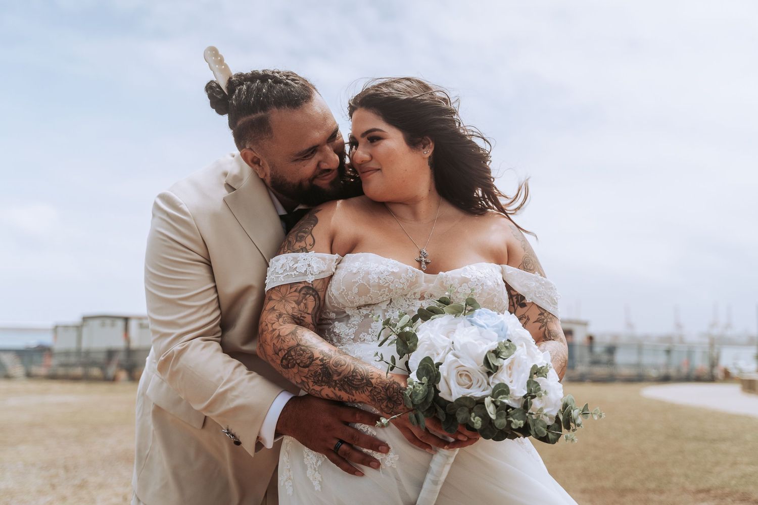 Intimate moment between newlyweds with white floral bouquet against beige background.