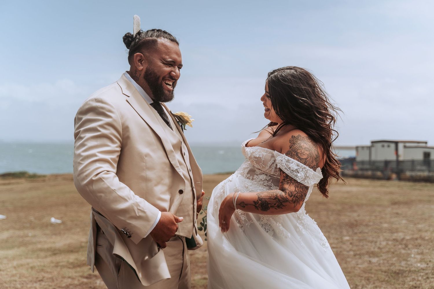 Joyful wedding couple laughing together during outdoor coastal ceremony.