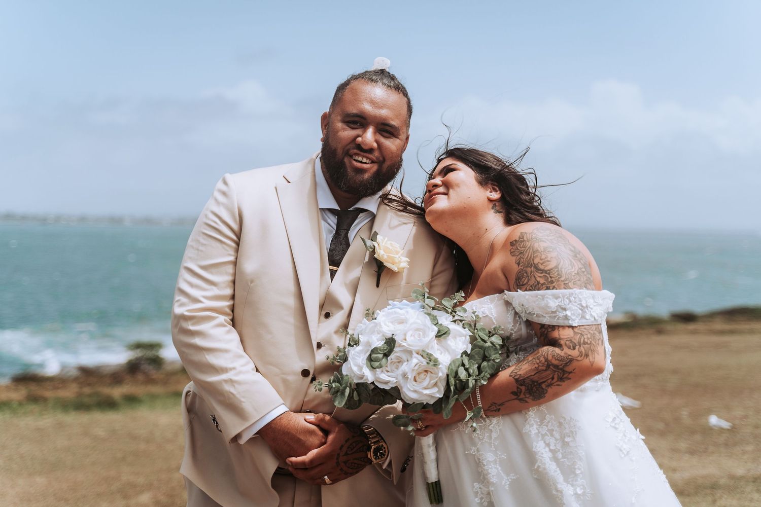 Happy couple sharing laughter during windy beach wedding with ocean backdrop.