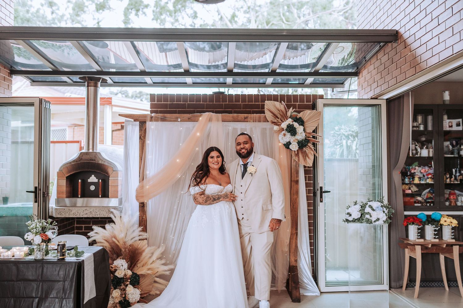 A romantic wedding ceremony setup in a sunroom with white drapery, floral arch, and rustic decor.