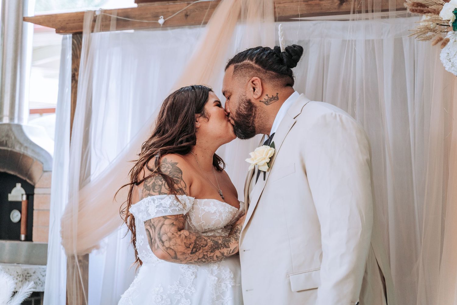 Intimate wedding moment captured under white drapes with floral decorations.