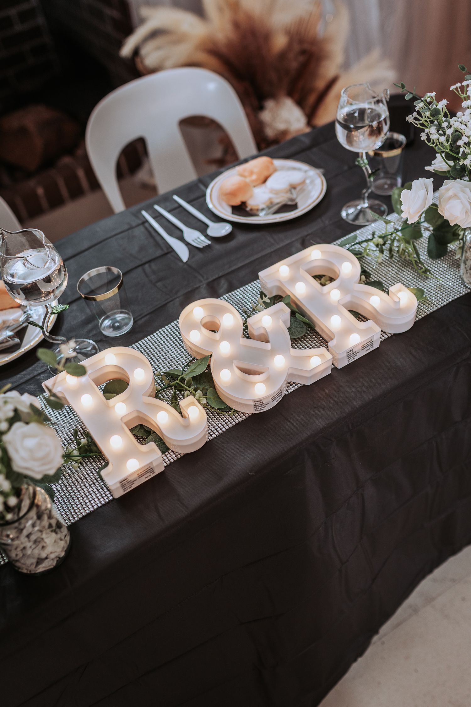 Wedding reception table with illuminated marquee letters spelling 'R&R' and elegant table settings.