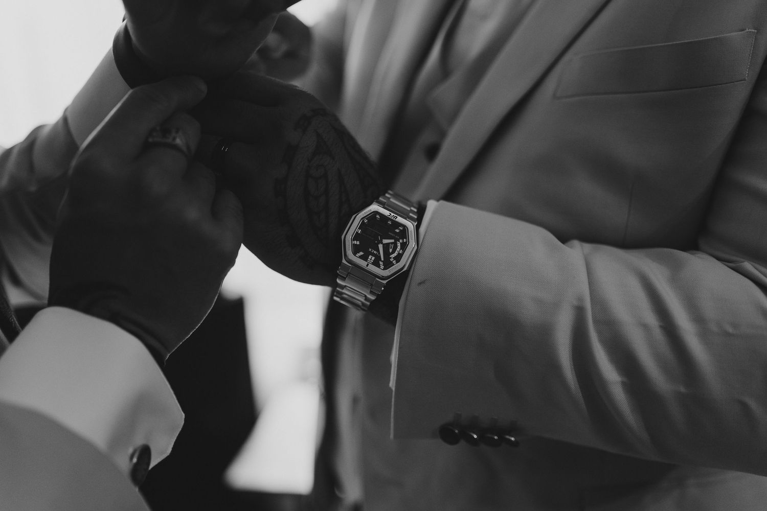 Close-up black and white detail shot of a luxury watch on a suited arm.