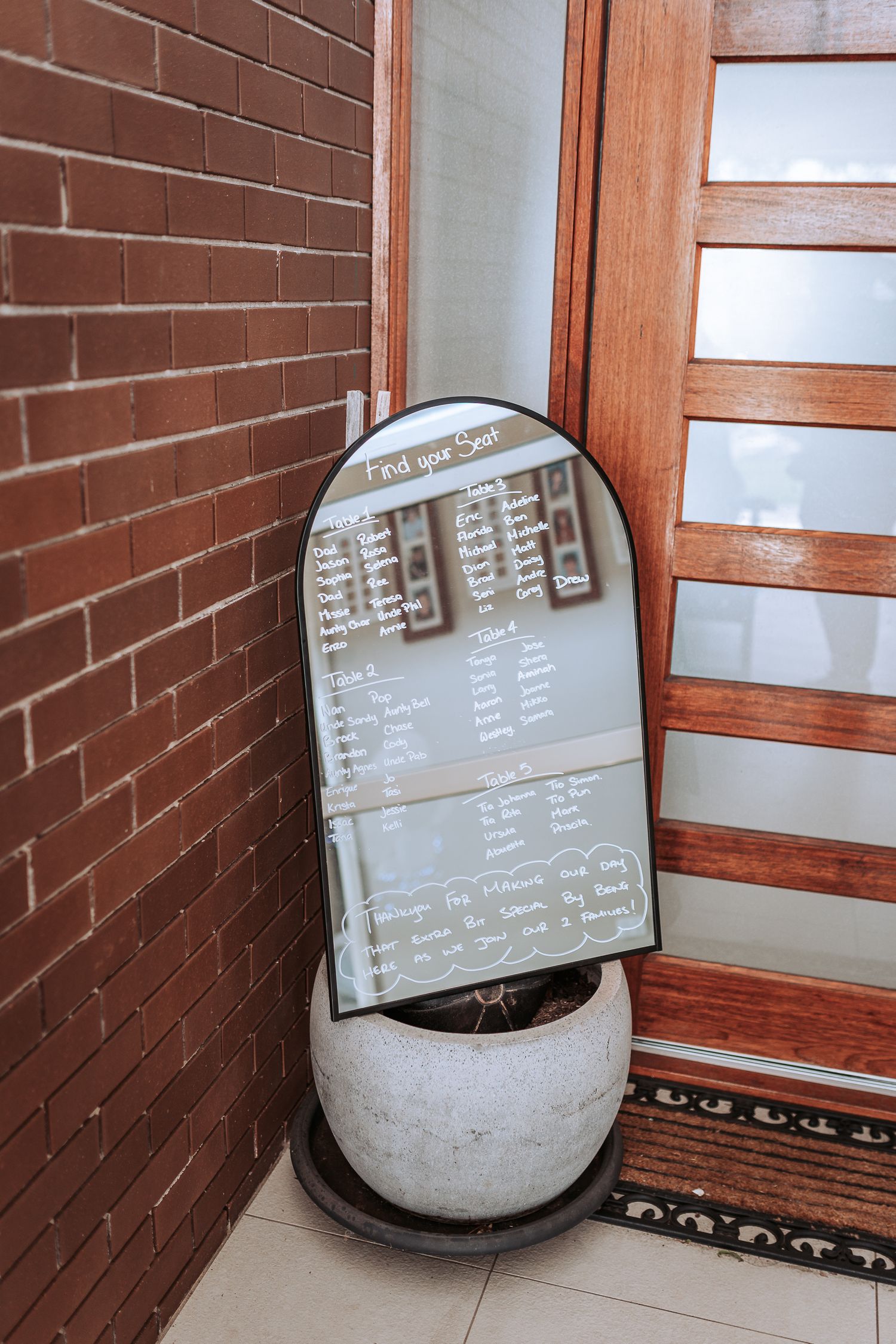 Mirror seating chart display against brick wall with concrete planter base.