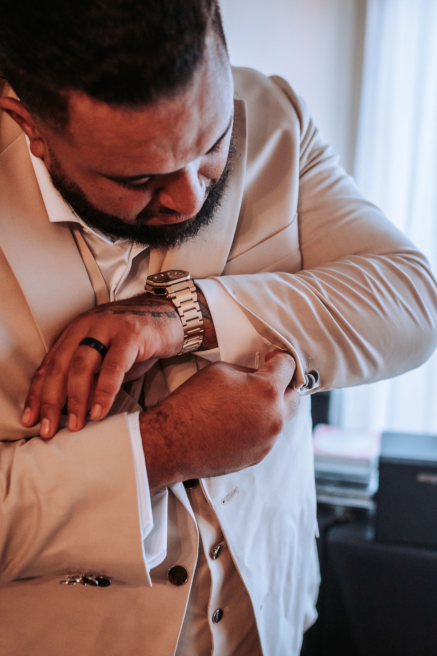 Close-up shot of someone adjusting their gold watch while wearing a beige suit.