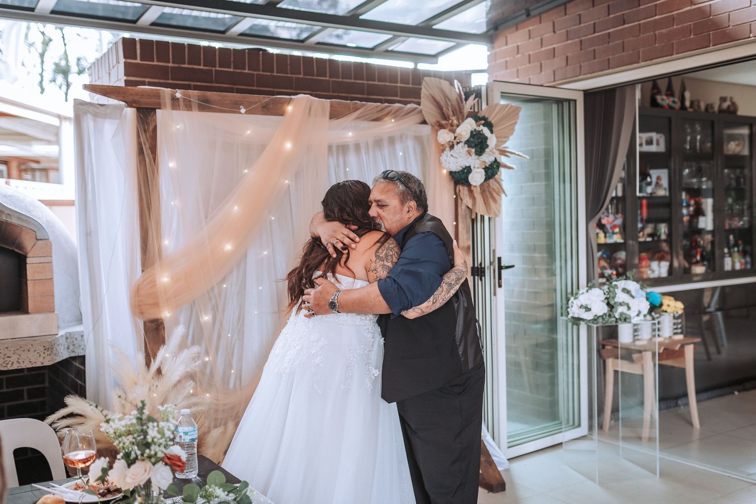 A tender moment between newlyweds beneath white draping and floral decorations at their reception.