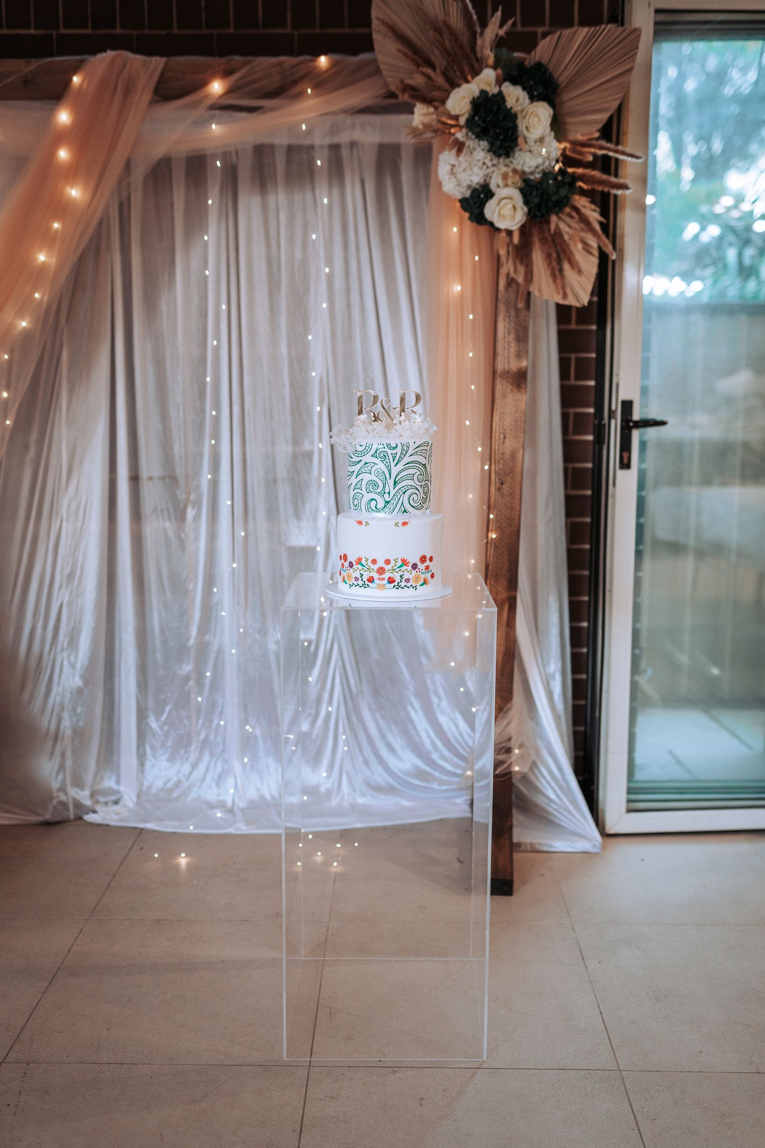 Elegant white wedding cake display with fairy lights and floral decorations against draped white fabric.