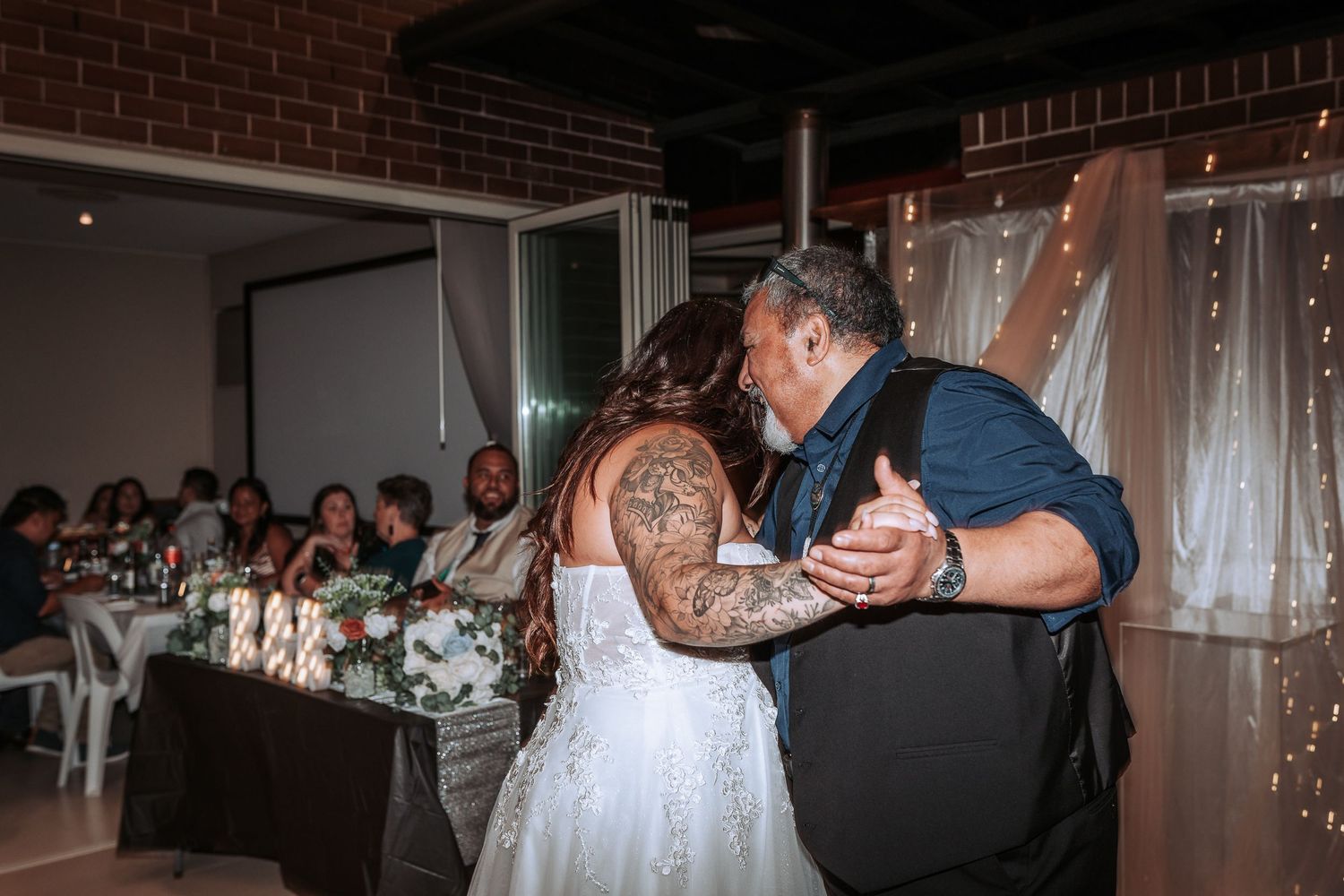 Couple sharing an intimate dance moment at a wedding reception with white decor and twinkle lights.