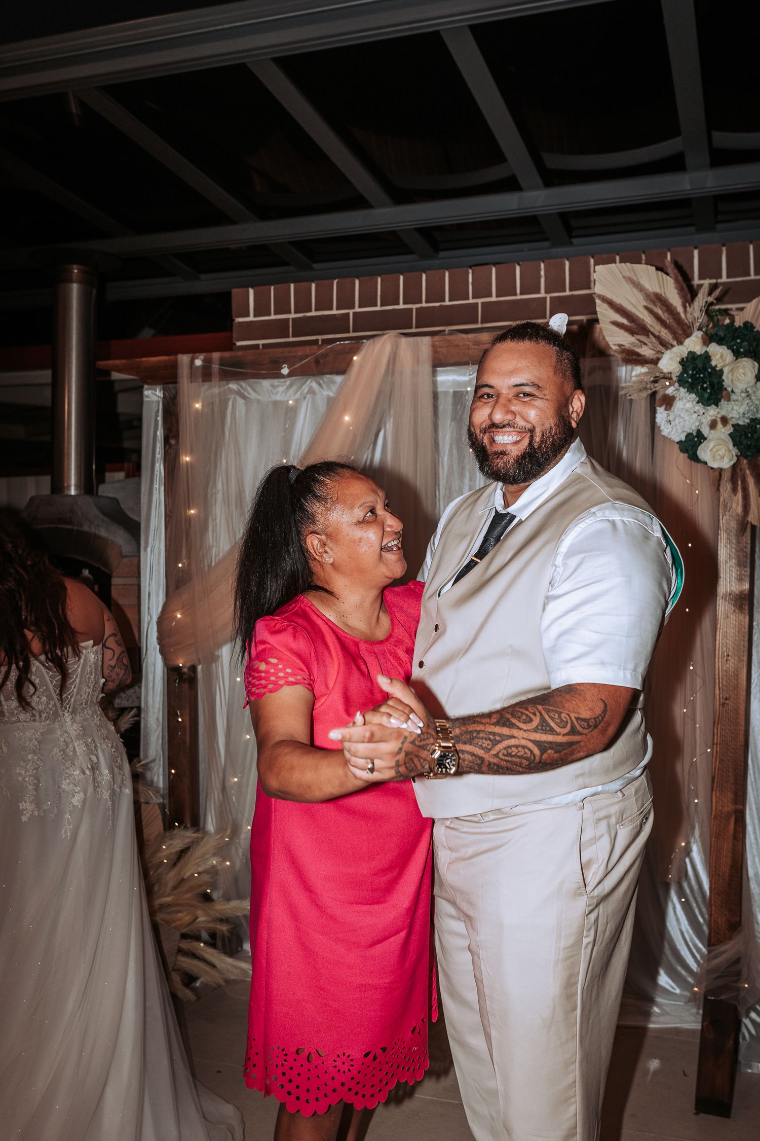 Wedding celebration dance with guests in elegant attire against a brick wall backdrop.