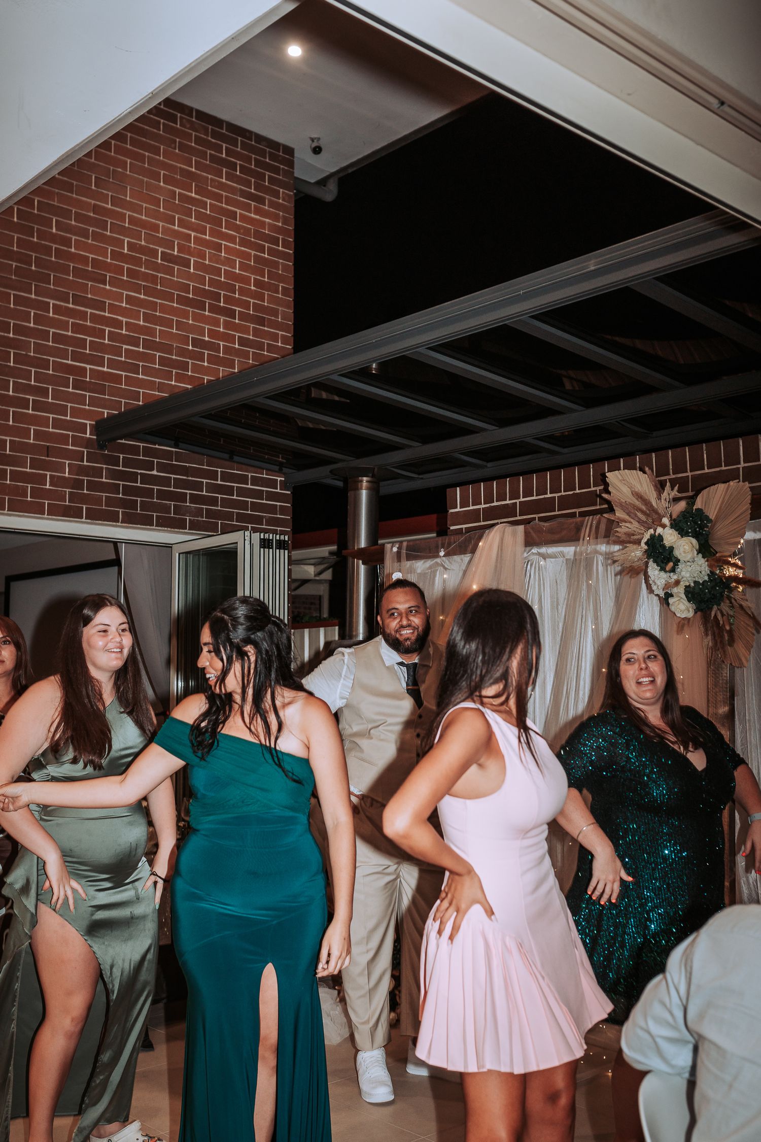 Wedding celebration with guests dancing in formal attire at an indoor reception venue.