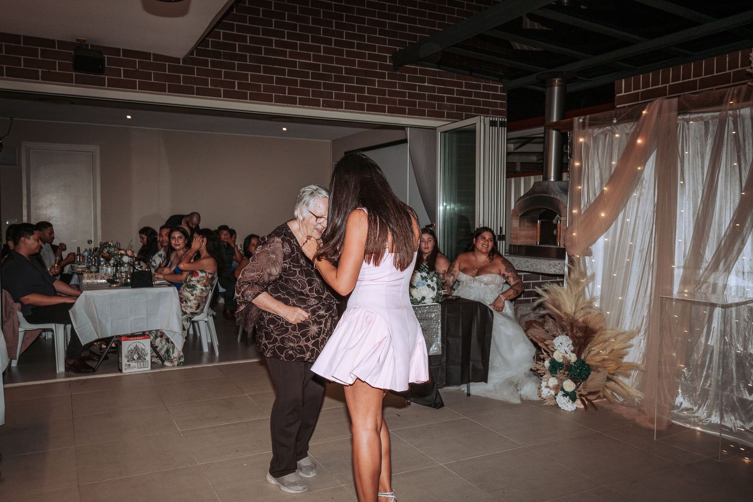 Two people sharing a dance at a wedding reception with guests seated in the background.