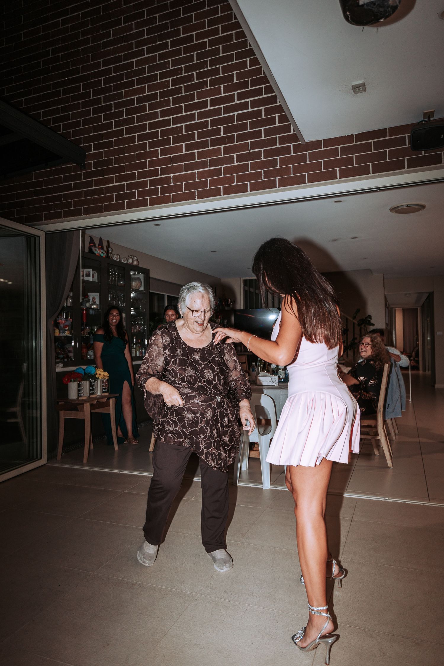 Two people dancing together at an indoor wedding reception with brick walls.