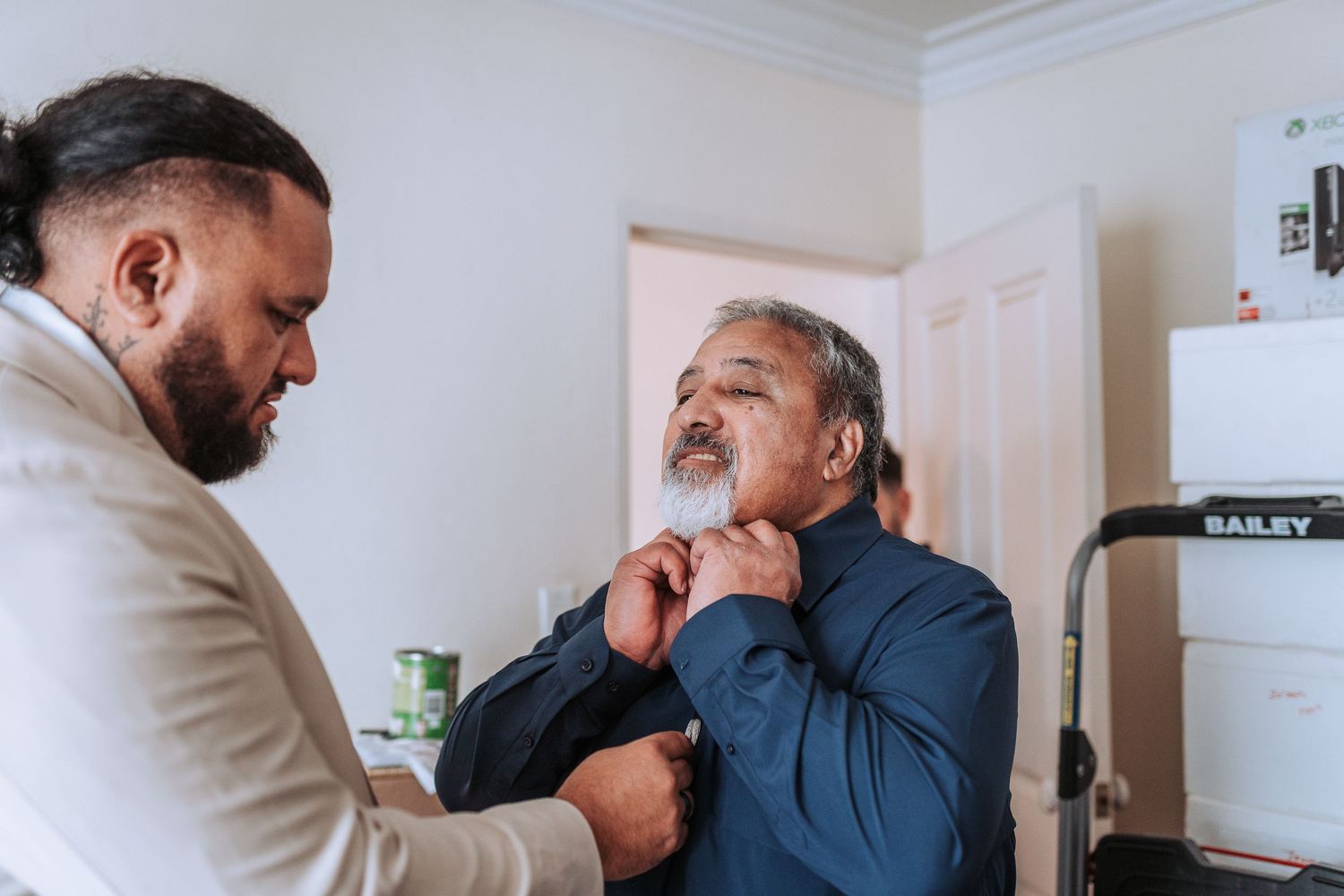 A moment of preparation before the wedding as a tie is being adjusted in a bright room.