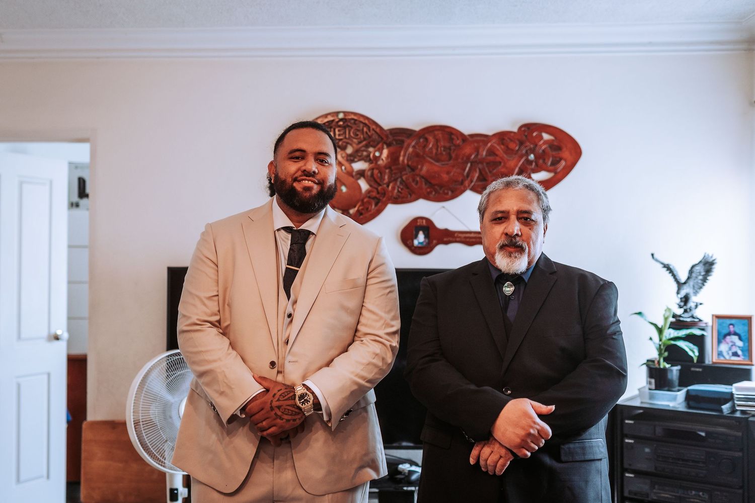 Two people in formal attire stand in a room with decorative wall art.