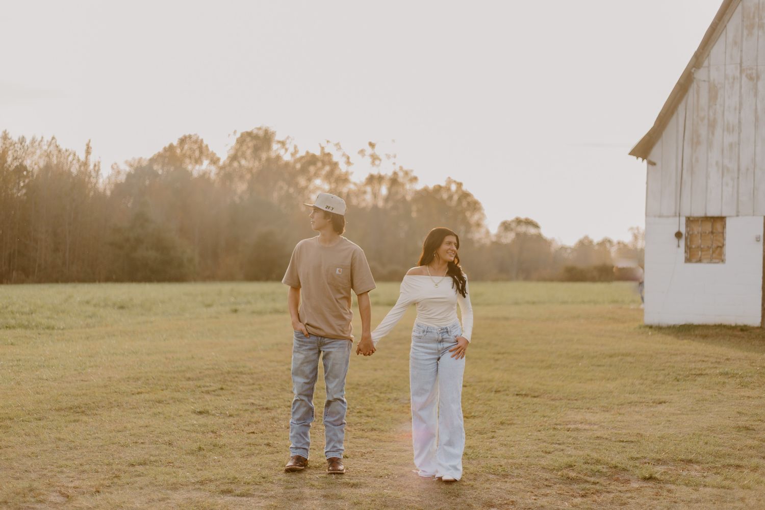 A couple poses together in white outfits against stone pillars and autumn trees during a golden hour photoshoot.