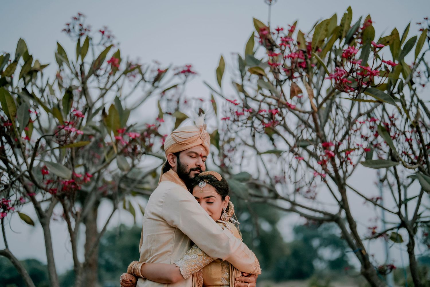 A joyful couple in traditional Indian wedding attire raise their hands together during a celebratory moment.