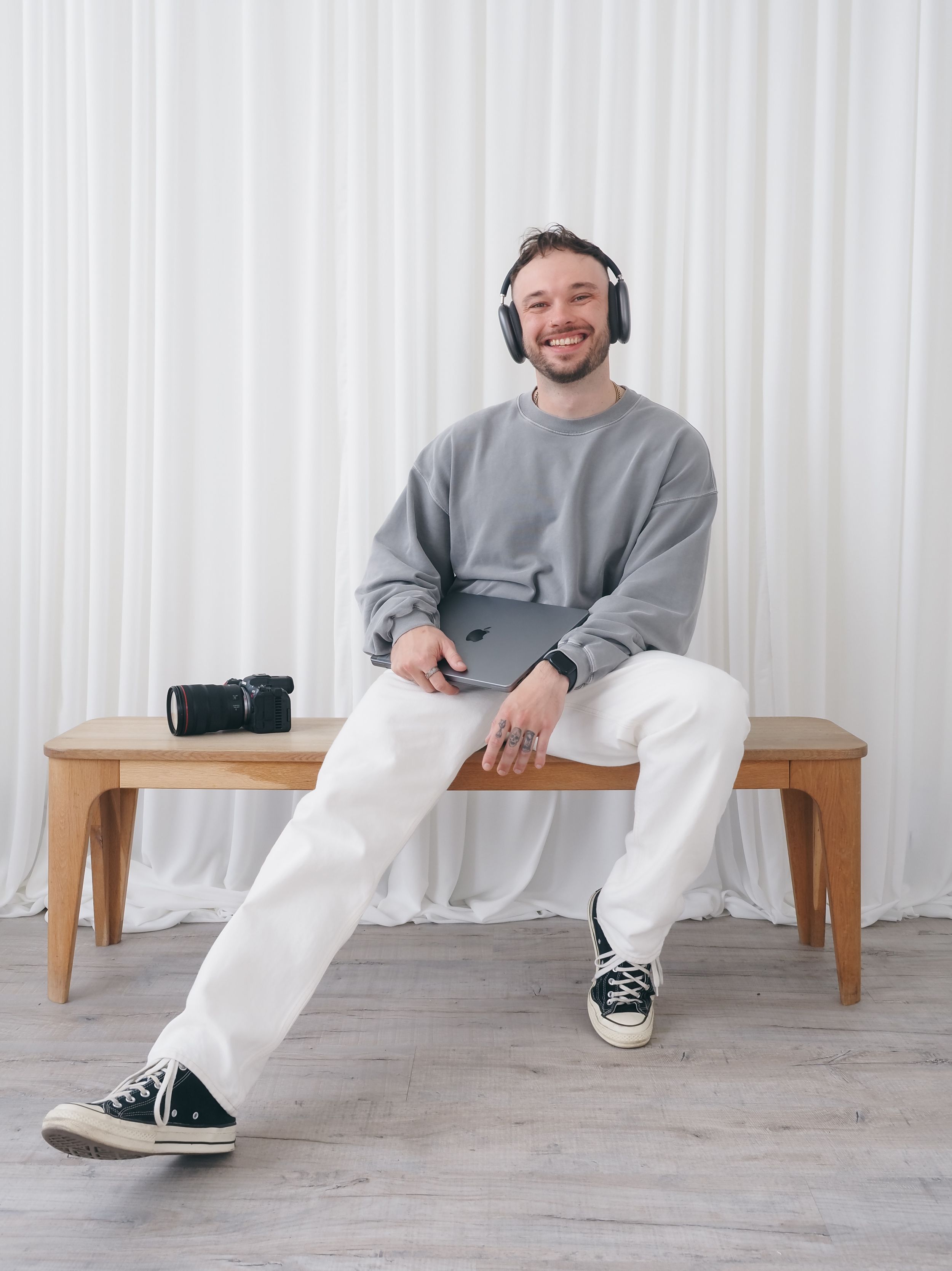 Person wearing grey sweatshirt and headphones sitting on wooden bench in studio setting.
