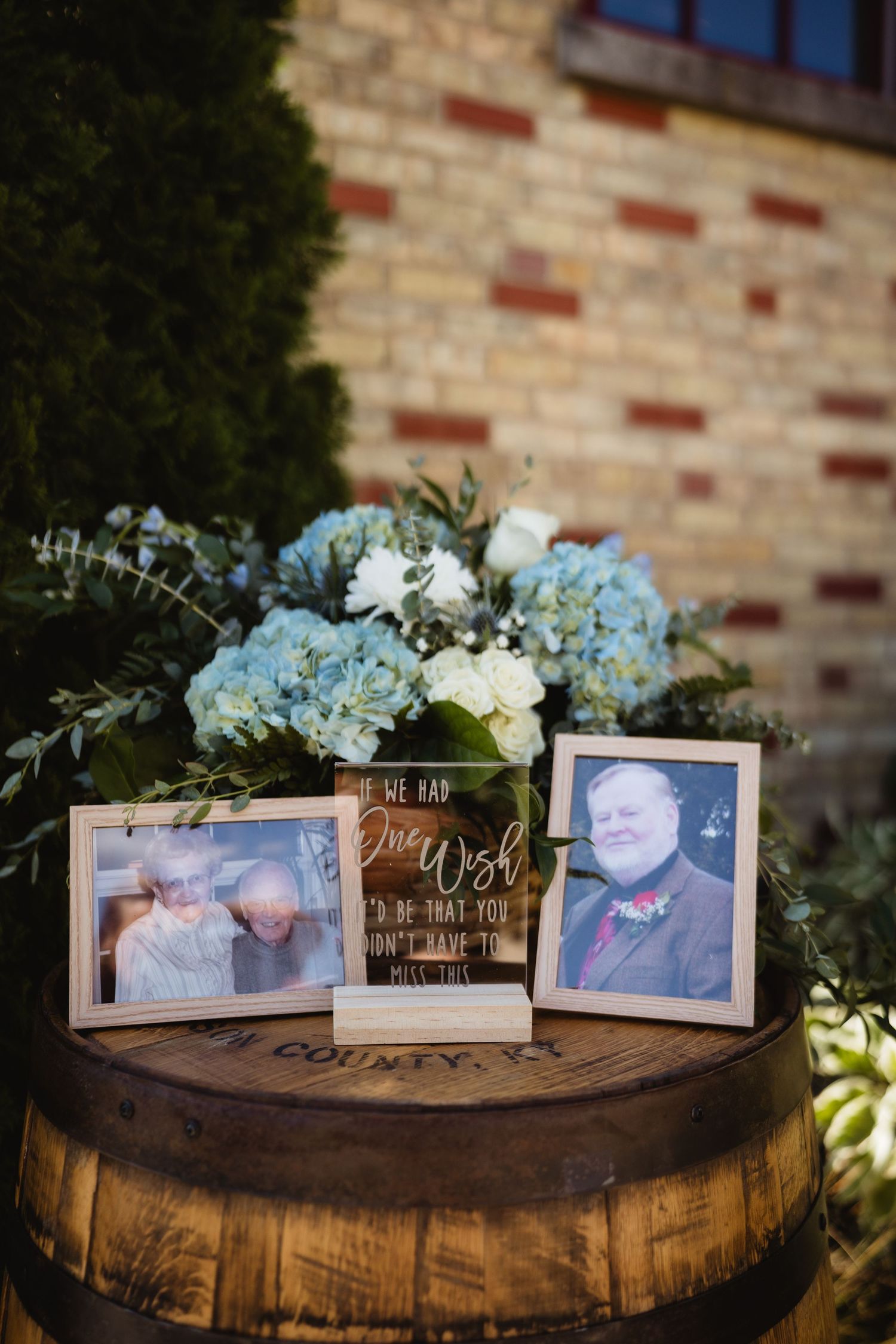 A series of photo frames displayed on a rustic wooden barrel with blue hydrangeas and floral decor.