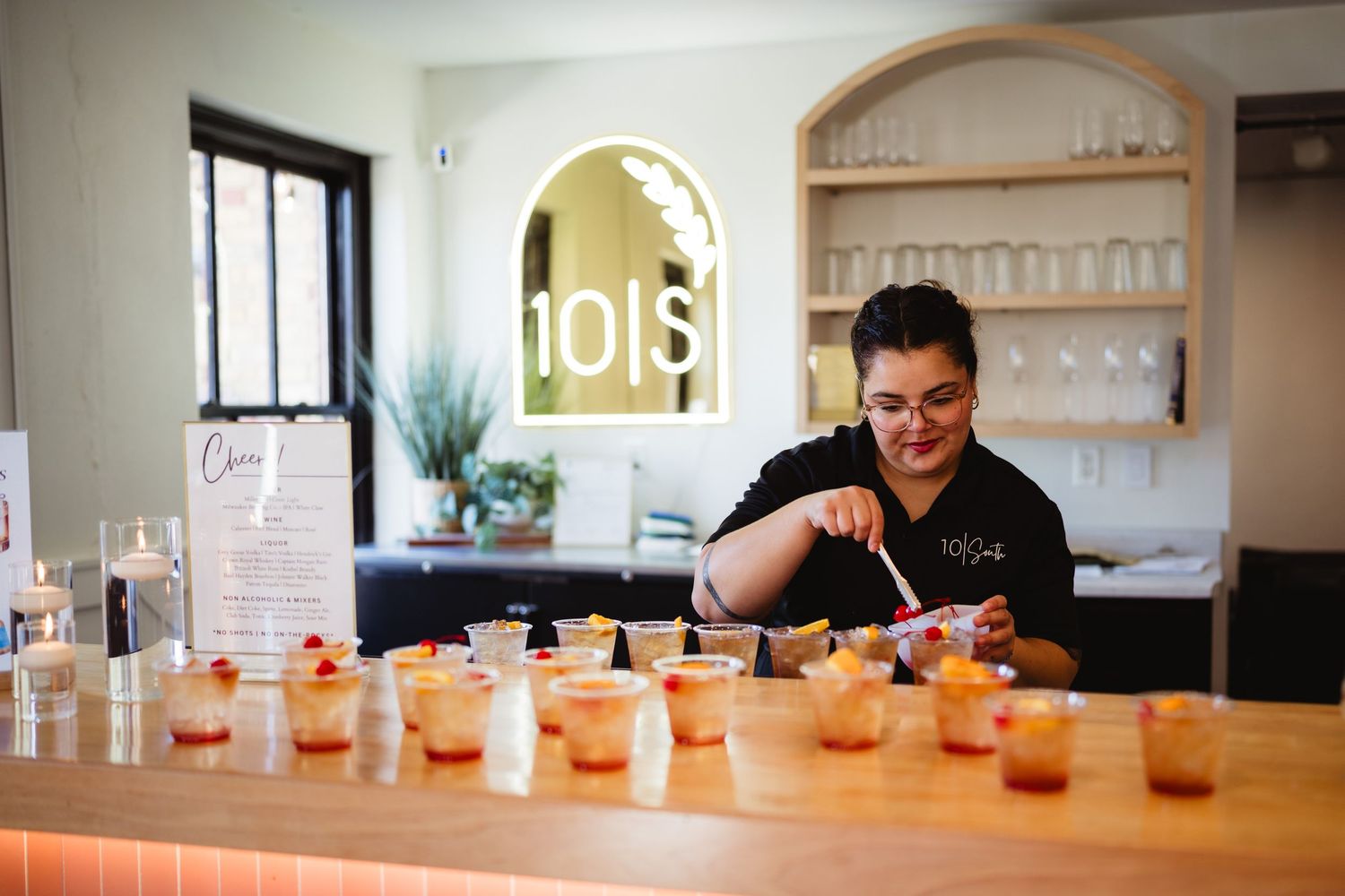 A row of orange cocktails lined up on a wooden bar counter with bartender in background.