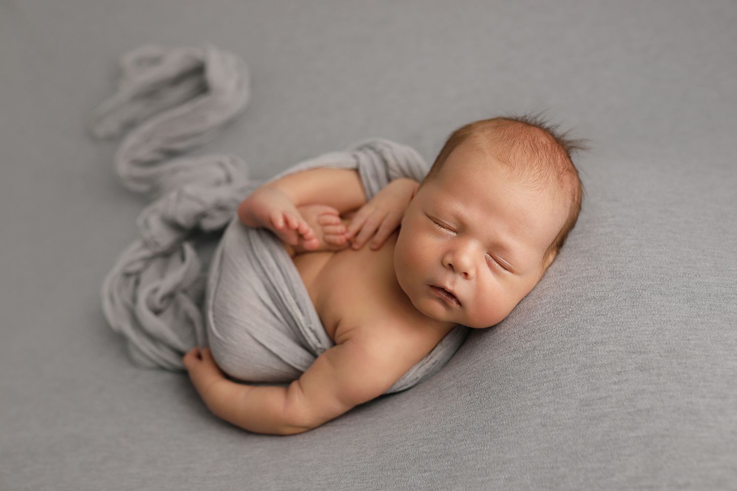 Newborn baby sleeping peacefully on soft gray blanket in artistic black and white portrait series.