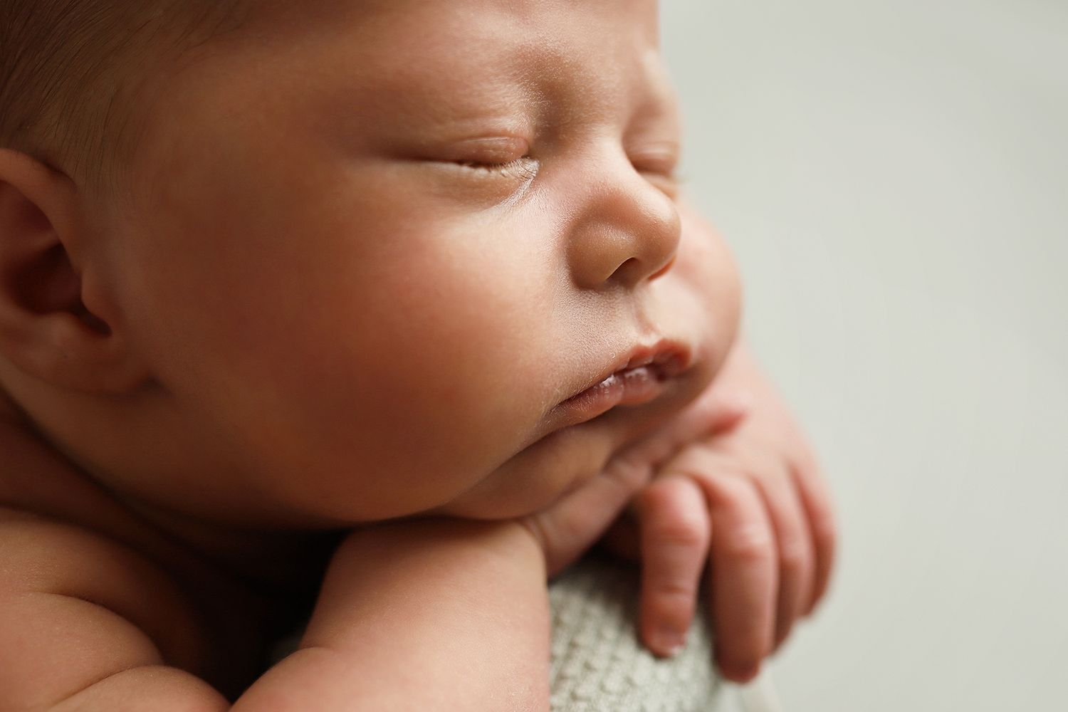 A sleeping newborn baby rests peacefully with tiny fingers curled near their face.