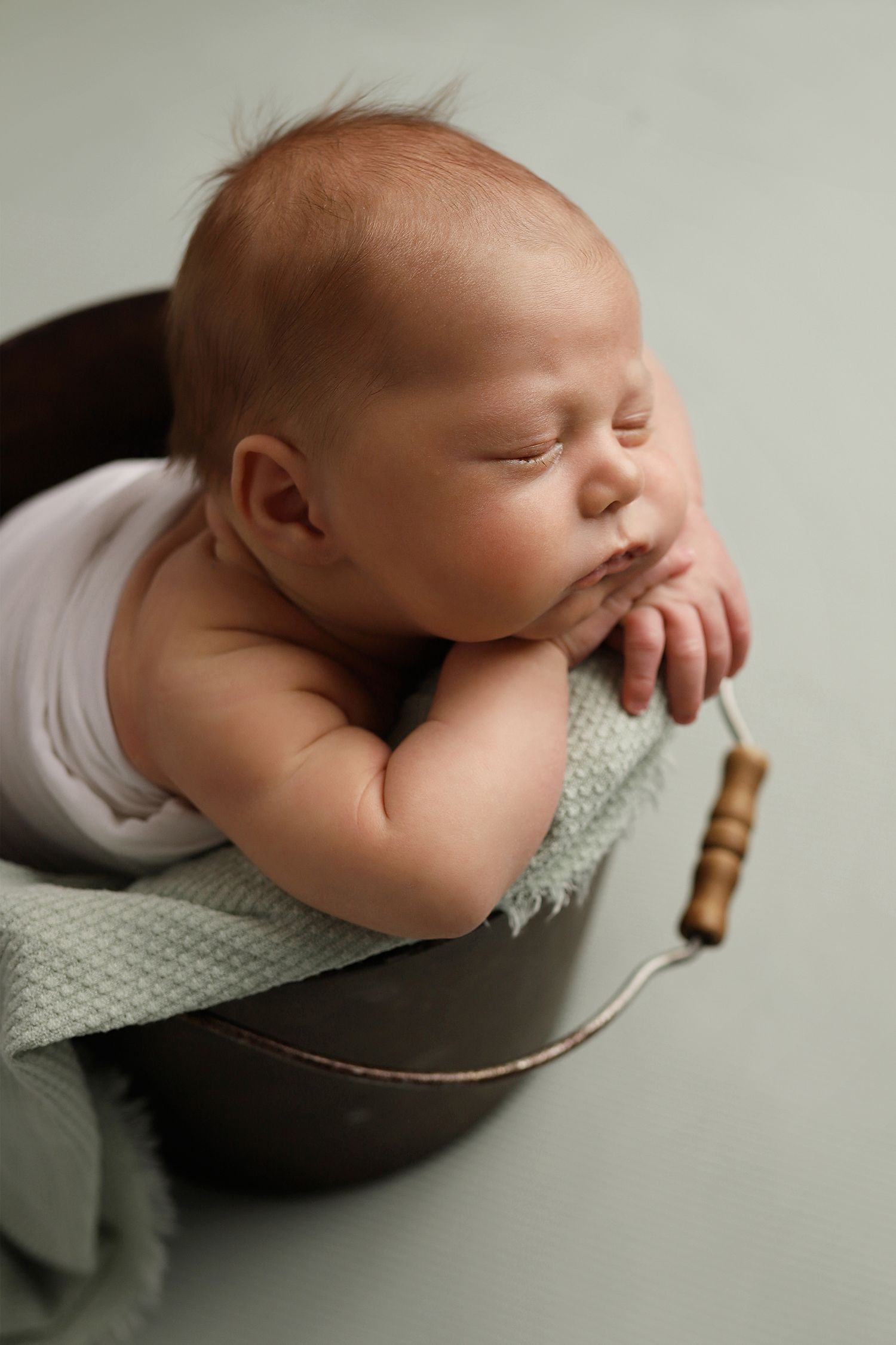 A sleeping newborn baby rests peacefully on a dark cushion with a knitted blanket and rustic wooden prop.