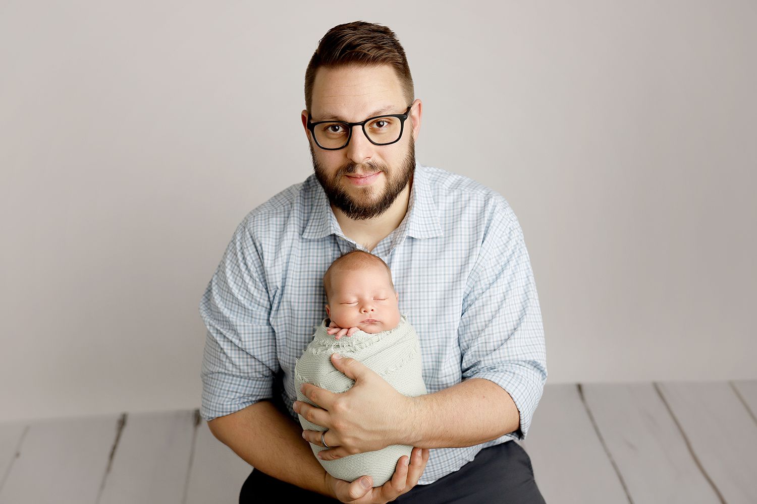 A series of photos showing a parent in glasses and beard holding a sleeping newborn baby against a light gray background.