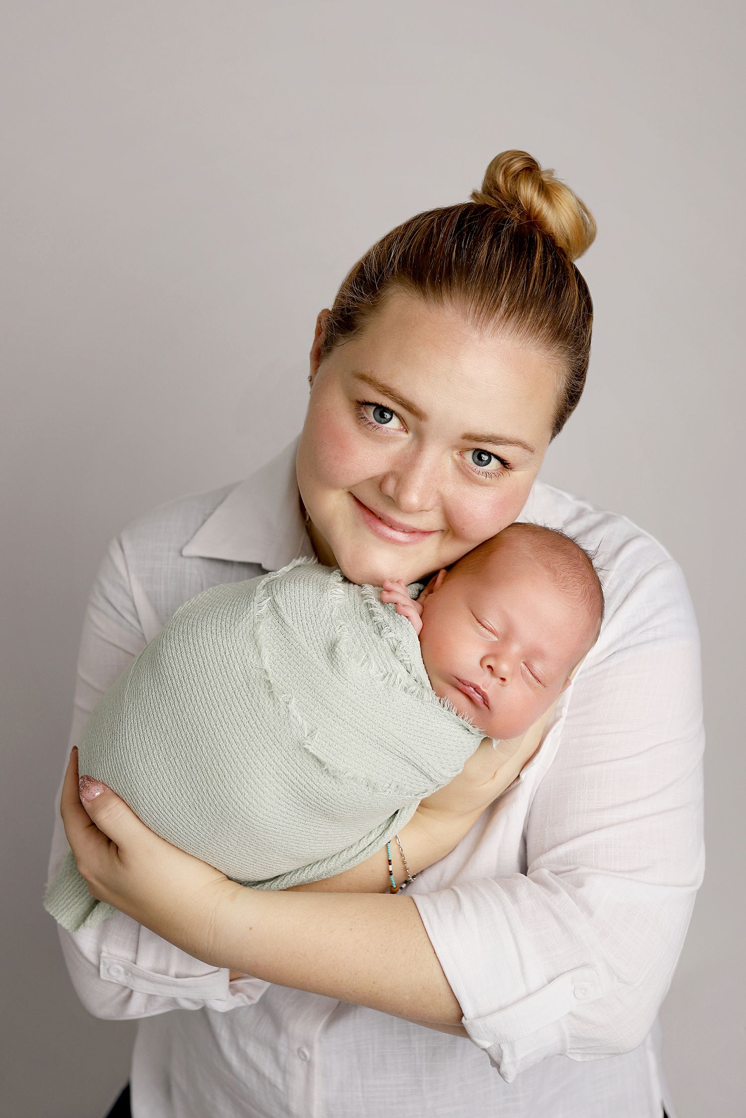 A series of tender moments showing a baby in mint green being cradled and embraced against a light gray background.