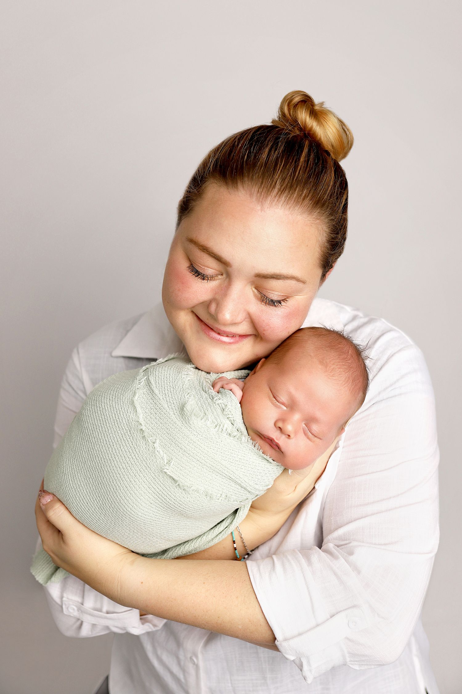 A series of tender moments showing a parent cuddling with a baby wrapped in a mint green blanket against a white backdrop.