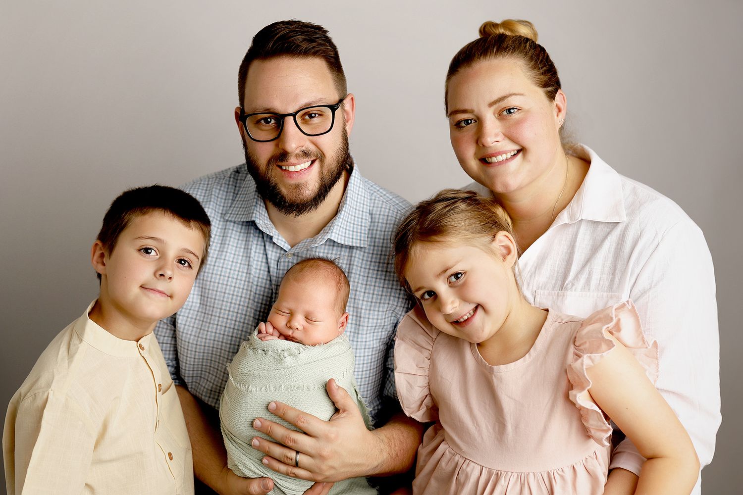A family of five poses together for a studio portrait against a neutral gray background.