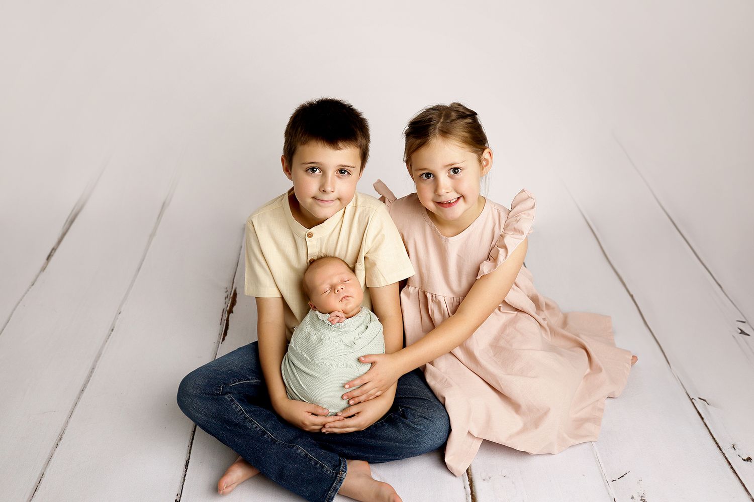 Two children sit together on a white wooden floor in casual clothing.