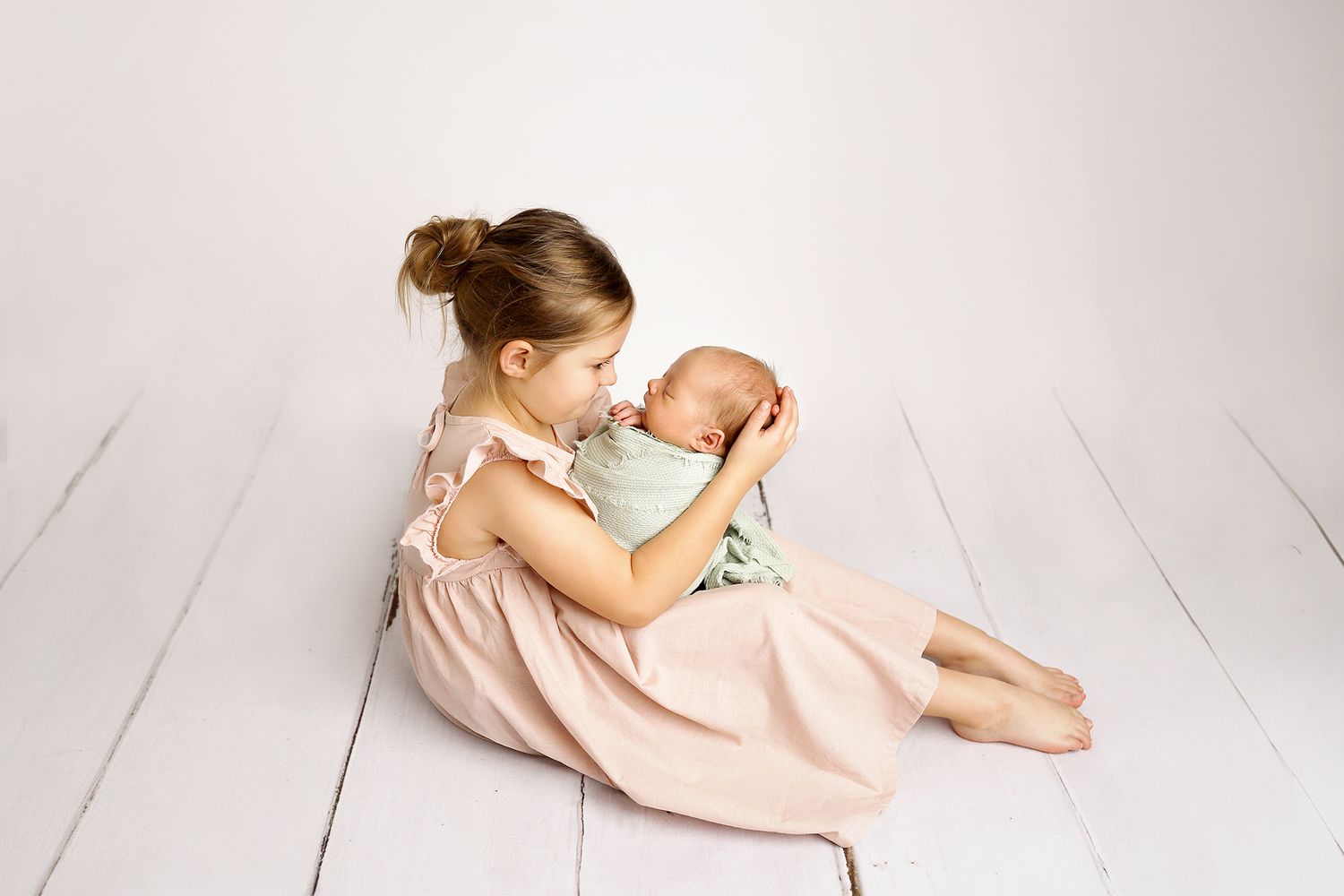 Two siblings cuddle and laugh while lying on a white wooden floor.