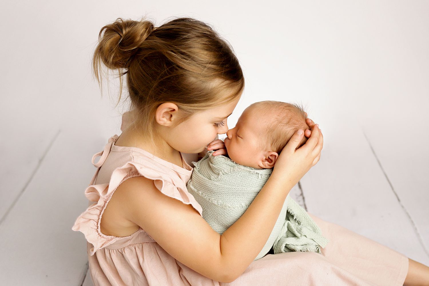 Sweet bonding moments captured between a baby in mint green and caregiver in soft lighting against white backdrop.