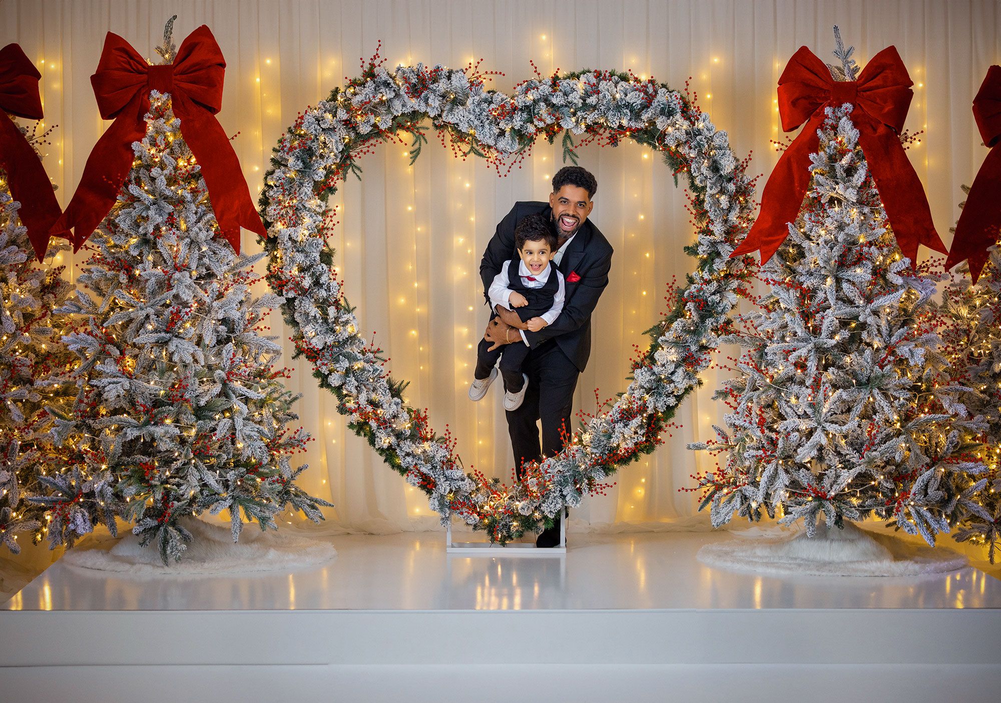 Elegant holiday display with flocked Christmas trees, red bows, and heart-shaped arch illuminated by twinkling lights.