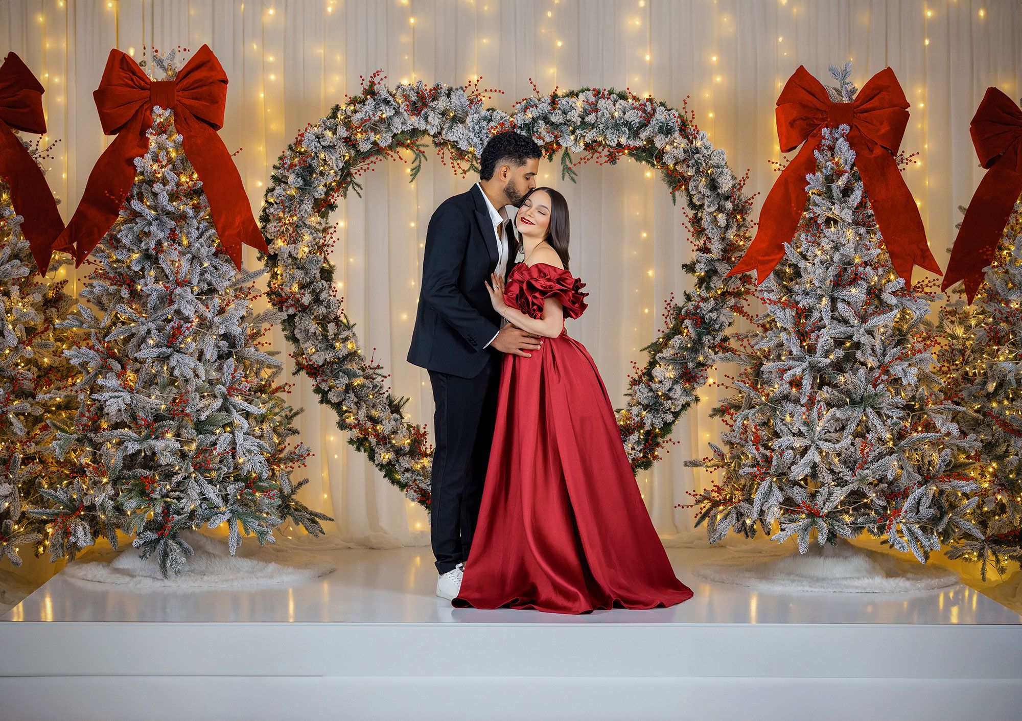 Festive holiday photo session with flocked Christmas trees, red bows, and twinkling lights creating a magical backdrop.