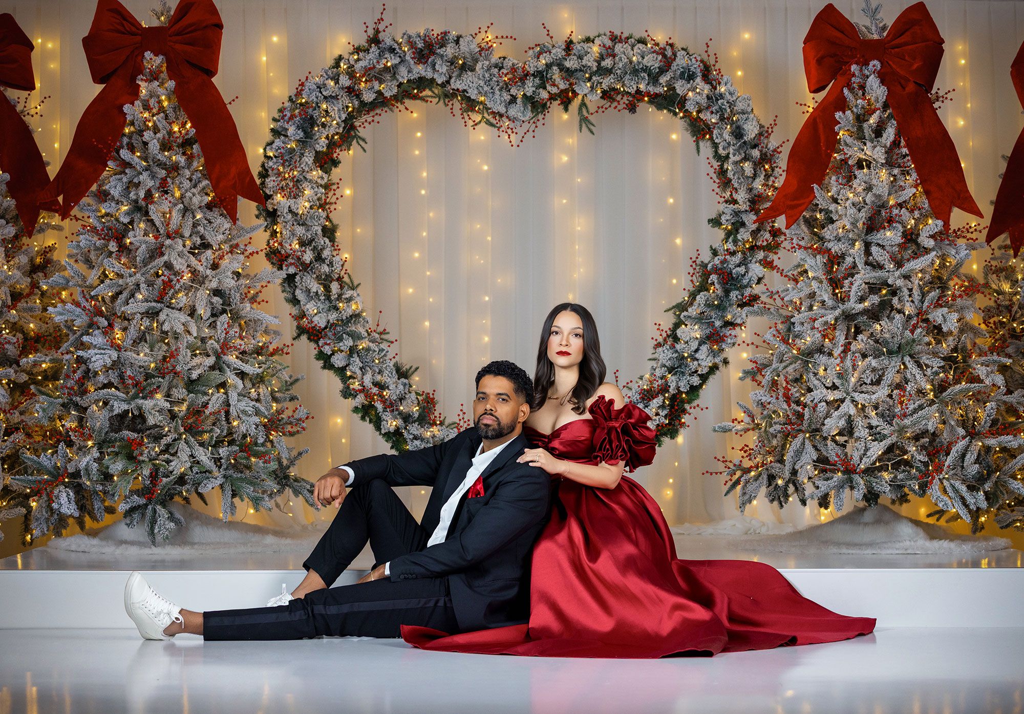 Elegant holiday photo setup with silver wreaths, red bows, and twinkling lights creating a festive backdrop.