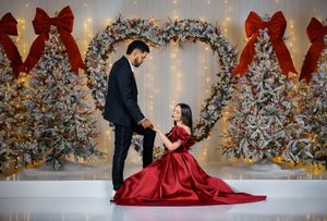 Elegant couple poses against a winter wonderland backdrop with silver trees and red holiday decor.