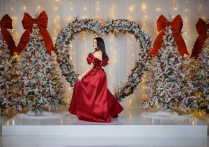 Romantic holiday photoshoot featuring a flowing red dress against frosted Christmas trees and string lights.