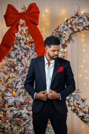 Sophisticated portrait of man in black suit against silver Christmas trees and twinkling lights.