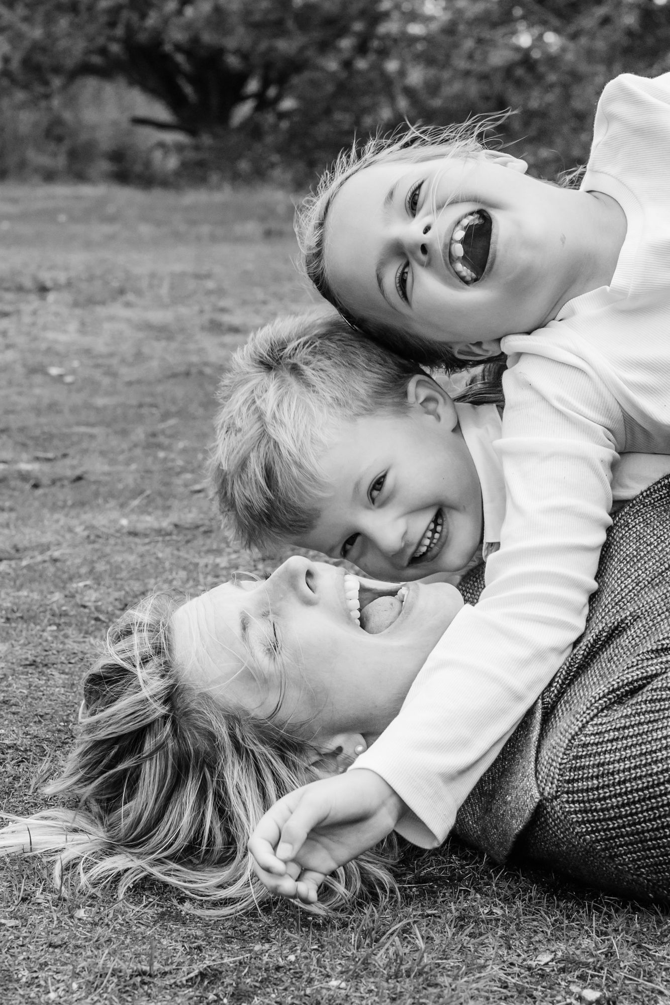 Black and white photo series showing playful moments lying in grass with natural expressions and candid poses.