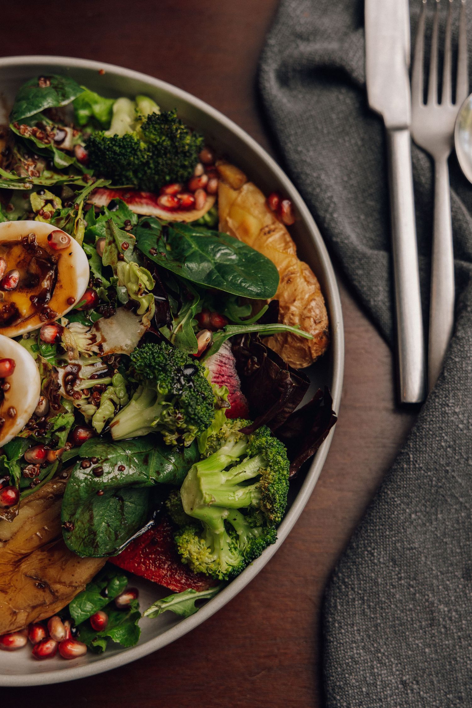 Fresh salad with broccoli, pomegranate seeds and mixed greens served on gray plates.