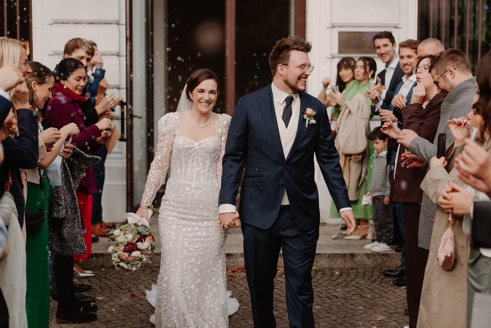 Newlywed couple walks through crowd of guests tossing flower petals during wedding ceremony exit.