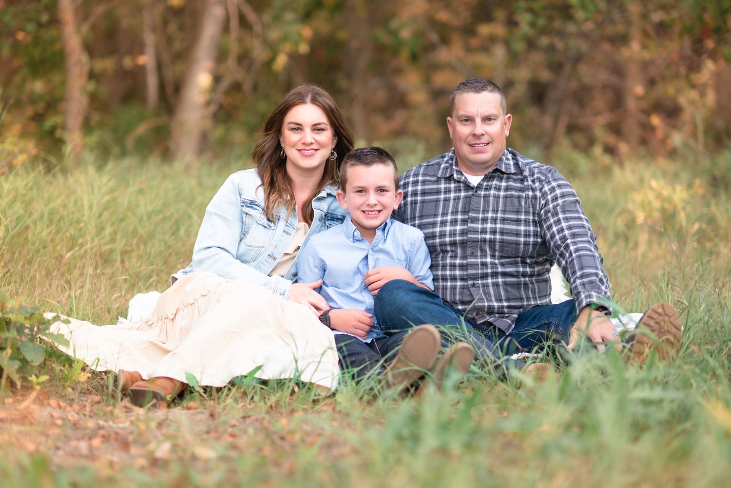 A family relaxes together outdoors on a blanket during an autumn photo session in a grassy field.