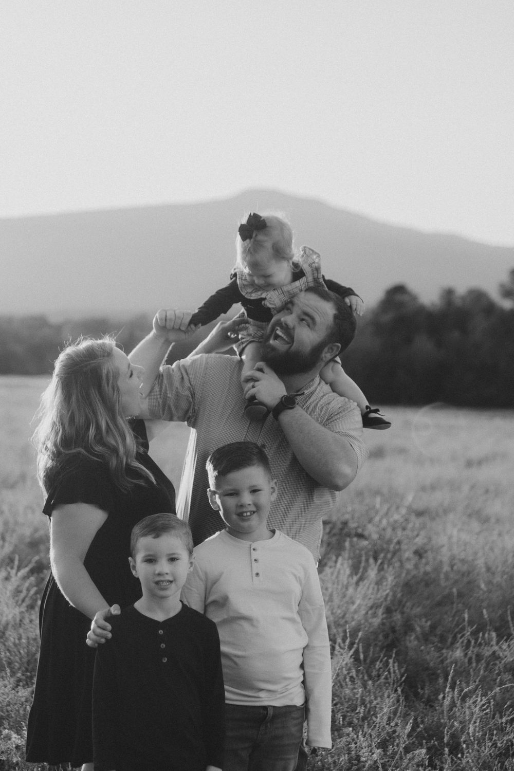 A series of candid black and white family photos showing joyful moments together in an outdoor field setting.