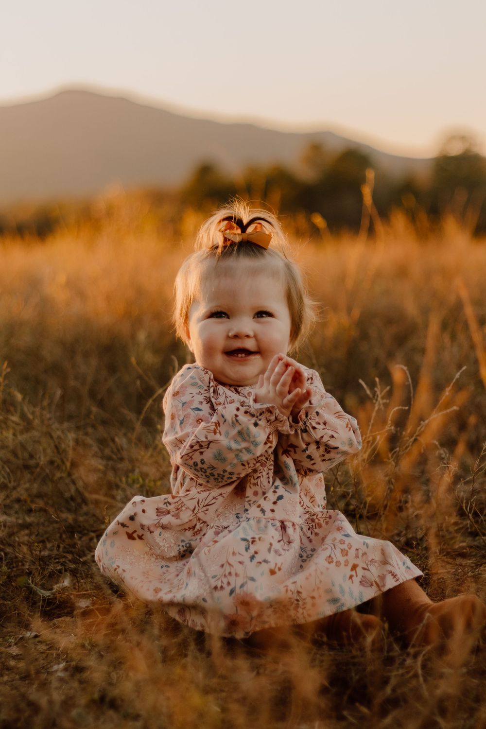 A small child in a white lace dress sits in a golden field at sunset, creating a dreamy outdoor portrait.