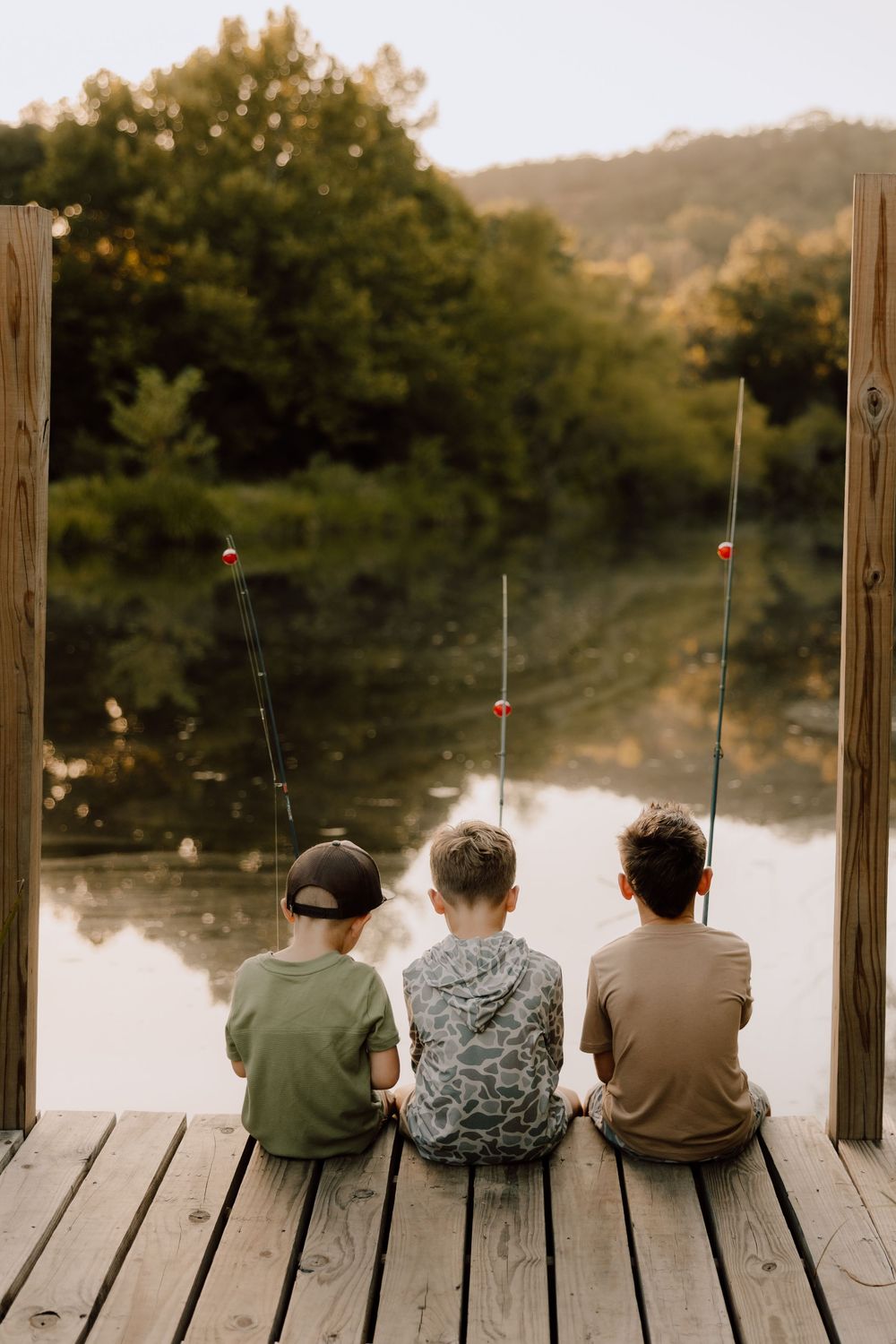 A group of people sit together on a wooden dock overlooking a peaceful lake at sunset.
