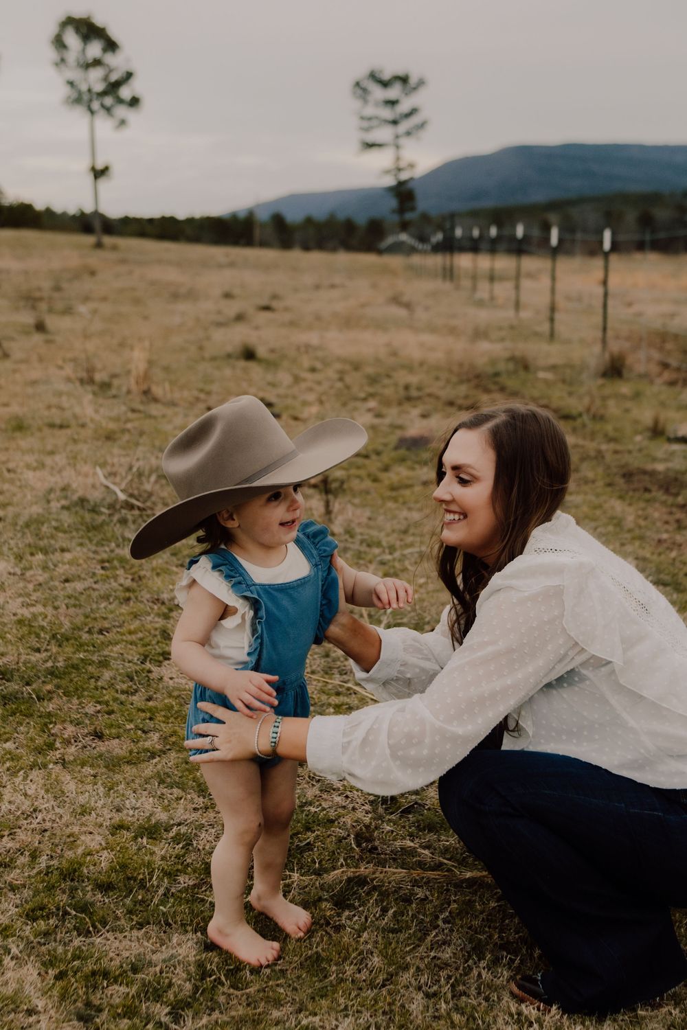 A tender moment shared between parent and child playing together in a grassy field on a cloudy day.